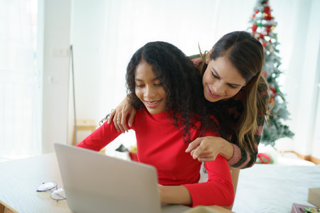 Caucasian white and African black ethnic women using laptop - notebook computer and having a discussion together in the room. Young woman colleagues working together on laptop computer.の写真素材