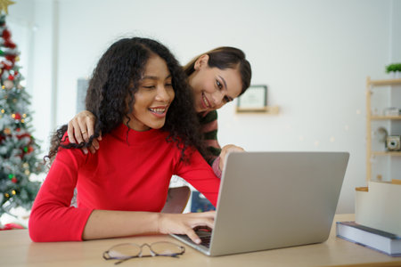 Caucasian white and African black ethnic women using laptop - notebook computer and having a discussion together in the room. Young woman colleagues working together on laptop computer.の写真素材