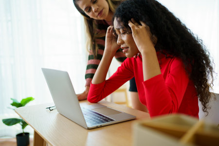 Unhappy - worried young woman expressing an unwell face in front of the notebook computer and her friend come to encourage her.の写真素材