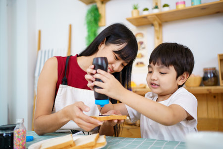 Happy little young boy and his mother making an easy breakfast together in a kitchen with a breads and chocolate jam. Mother and son playing together while making a breakfast.の写真素材