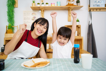 Happy little young boy and his mother making an easy breakfast together in a kitchen with a breads and chocolate jam. Mother and son playing together while making a breakfast.の写真素材