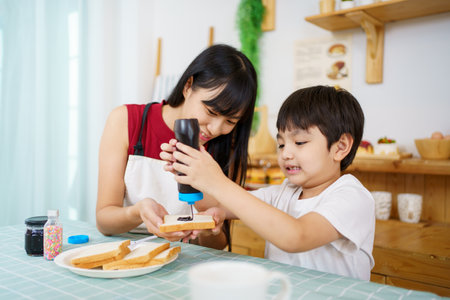 Happy little young boy and his mother making an easy breakfast together in a kitchen with a breads and chocolate jam. Mother and son playing together while making a breakfast.の写真素材