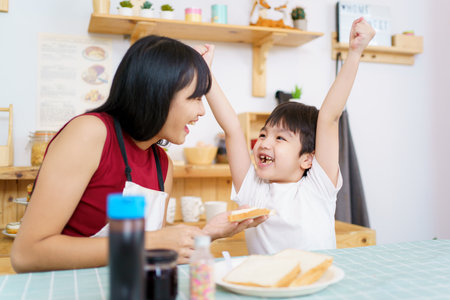 Happy little young boy and his mother making an easy breakfast together in a kitchen with a breads and chocolate jam. Mother and son playing together while making a breakfast.の写真素材