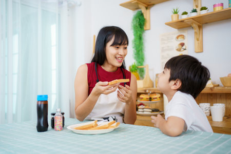 Happy little young boy and his mother making an easy breakfast together in a kitchen with a breads and chocolate jam. Mother and son playing together while making a breakfast.の写真素材