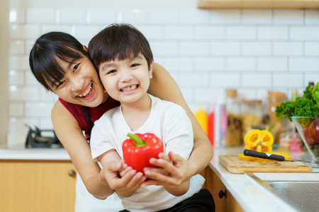 Happy cheerful mother and her little boy preparing a foods and vegetables in domestic kitchen together. Mother and son smiling and looking at the camera in kitchen.の写真素材