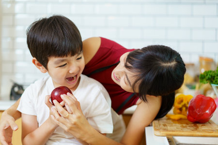 Happy cheerful mother and her little boy preparing a foods and vegetables in domestic kitchen together. Mother and son smiling and looking at the camera in kitchen.の写真素材