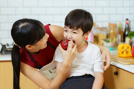 Happy cheerful mother and her little boy preparing a foods and vegetables in domestic kitchen together. Mother and son smiling and looking at the camera in kitchen.の写真素材