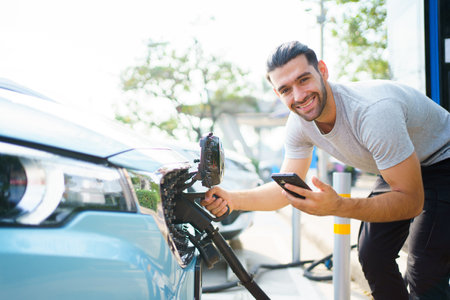 Handsome Asian young man holding an EV plug connector and attaching onto the car, man plugged in the EV charging connector to the vehicle.の写真素材
