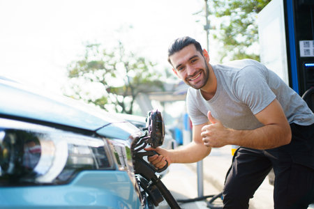 Handsome Asian young man holding an EV plug connector and attaching onto the car, man plugged in the EV charging connector to the vehicle.の写真素材