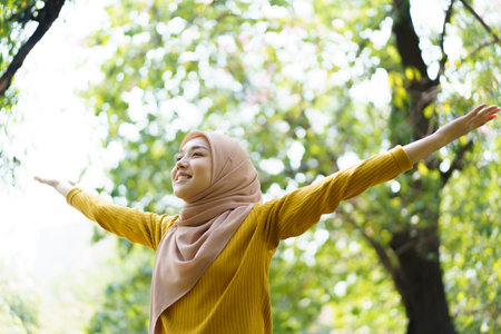 Happy cheerful Asian beautiful female muslim practicing an exercise and stretching at the park close up with copyspace. Modern muslim woman lifestyles and diversity concept.の写真素材