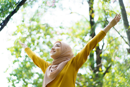 Happy cheerful Asian beautiful female muslim practicing an exercise and stretching at the park close up with copyspace. Modern muslim woman lifestyles and diversity concept.の写真素材