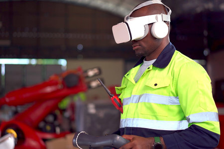 Professional robotic and manufacturing technician or engineer using a virtual reality - VR goggles and remote control to control an automated robotic arm.の写真素材