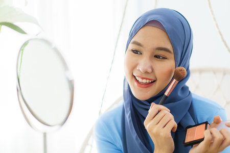 Modern lifestyles of female muslim people portrait, a beautiful Asian muslim woman applying a cosmetic and brushing her face. Modern muslim lifestyle concept.の写真素材