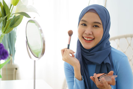 Modern lifestyles of female muslim people portrait, a beautiful Asian muslim woman applying a cosmetic and brushing her face. Modern muslim lifestyle concept.の写真素材