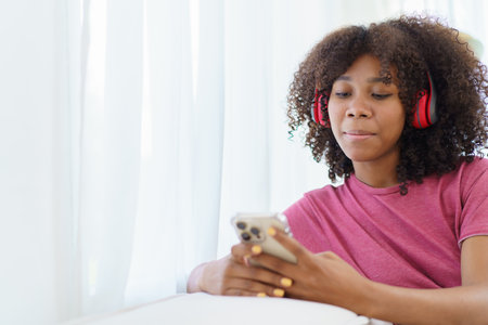 Happy cheerful American - African black teenager woman relaxing in the living room and using smartphone to browse the social network or internet. Woman relaxing in living room and using smartphone.の写真素材