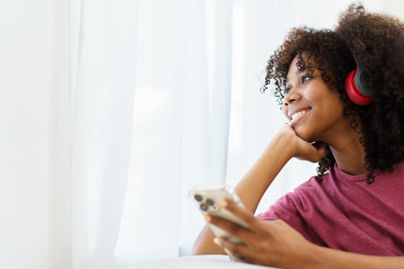 Happy cheerful American - African black teenager woman relaxing in the living room and using smartphone to browse the social network or internet. Woman relaxing in living room and using smartphone.の写真素材