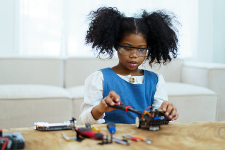 Happy cheerful American - African ethnicity girl enjoy learning to assemble a robot by herself. Creativity and thinkiing learning skill in elementary children.の写真素材