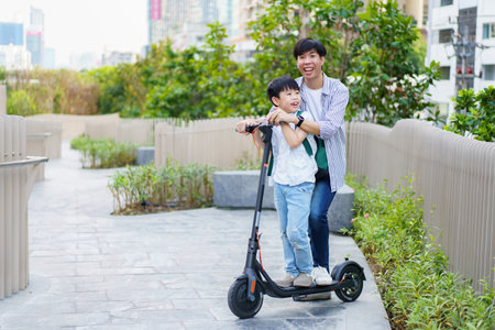 Happy cheerful Asian man and little boy riding an electric scooter in the city, Eco or green urban lifestyle traveling concept. Man and boy riding an electric scooter in city without safety helmet.の写真素材