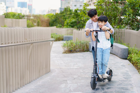 Happy cheerful Asian man and little boy riding an electric scooter in the city, Eco or green urban lifestyle traveling concept. Man and boy riding an electric scooter in city without safety helmet.の写真素材