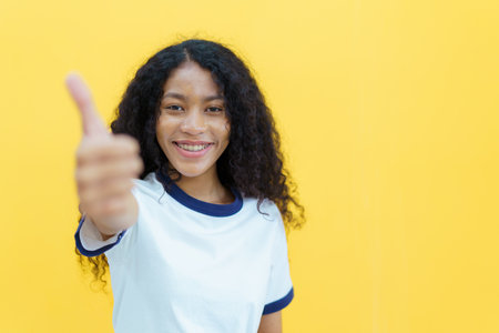 Confident happy black woman smiling to camera portrait on yellow background. Close up portrait of beautiful young black woman smiles and crossed arms.の写真素材
