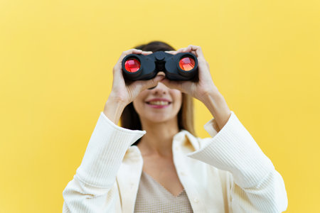 Beautiful caucasian white young woman looking through the twin lens binocular. Woman using binocular portrait on yellow background.の写真素材