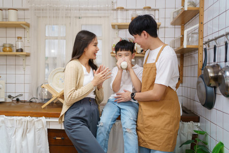 Asian cute little boy having a breakfast with his parent in a kitchen, boy holding a glass of milk and drink.の写真素材