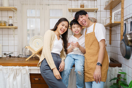 Asian cute little boy having a breakfast with his parent in a kitchen, boy holding a glass of milk and drink.の写真素材