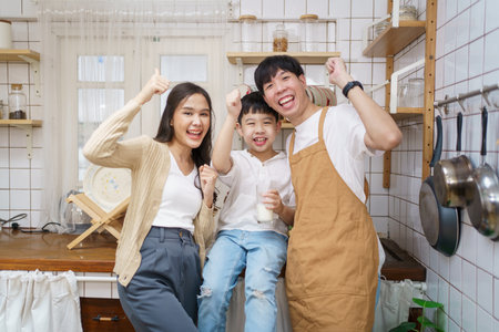 Asian cute little boy having a breakfast with his parent in a kitchen, boy holding a glass of milk and drink.の写真素材