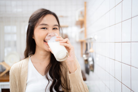 Beautiful happy Asian woman drinking a milk in morning in kitchen and smiling to camera. Happy Asian woman shows a glass of milk and smiles.の写真素材