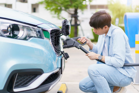 Handsome Asian young man holding an EV plug connector and attaching onto the car, man plugged in the EV charging connector to the vehicle.の写真素材