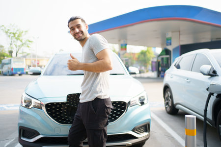 Handsome Asian young man holding an EV plug connector and attaching onto the car, man plugged in the EV charging connector to the vehicle.の写真素材
