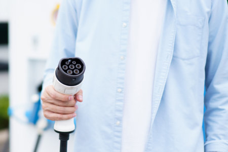 Unrecognizable Asian man holding AC type 2 EV charging connector at EV charging station, man preparing an EV - electric vehicle charging connector for recharge a vehicle.の写真素材