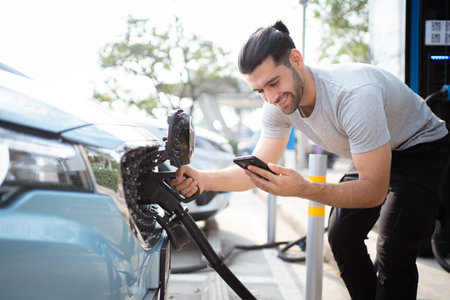 Handsome Asian young man holding an EV plug connector and attaching onto the car, man plugged in the EV charging connector to the vehicle.の写真素材