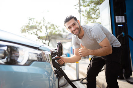 Handsome Asian young man holding an EV plug connector and attaching onto the car, man plugged in the EV charging connector to the vehicle.の写真素材