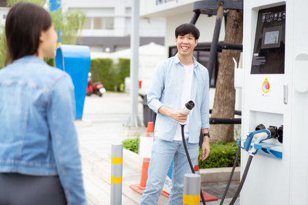 Asian man and woman holding AC type 2 EV charging connector at EV charging station. Road vehicle traveling or transportation with the clean energy concept.の写真素材
