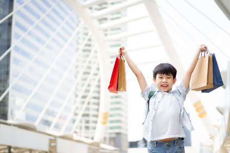 Cheerful happy Asian little boy carrying a paper shopping bags and smiling to camera.の写真素材