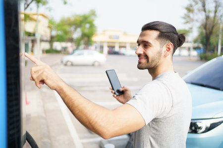 Cheerful happy Asian man using an EV charging application on smartphone to prepare vehicle charging and payment. Modern lifestyle of transportation with sustainability and sustainable energy.の写真素材