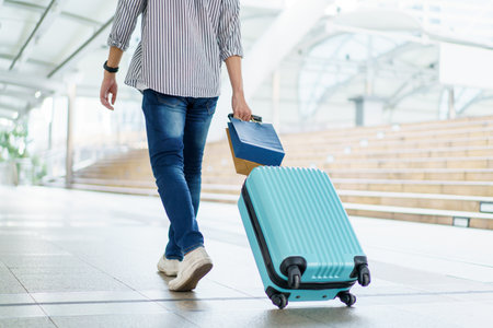 Asian young man dragging a suitcase along the city or airport terminal with shopping bags. Man traveling in the city or urban area.の写真素材