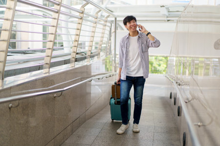 Asian young man dragging a suitcase along the city or airport terminal with shopping bags. Man traveling in the city or urban area.の写真素材
