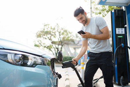 Handsome Asian young man holding an EV plug connector and attaching onto the car, man plugged in the EV charging connector to the vehicle.の写真素材