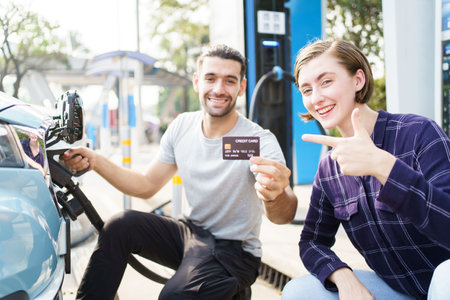 Lovely young caucasian couple charging their electric vehicle or EV car at fast charging EV station. Cashless or online payment for electric vehicle charging station. Sustainable energy concept.の写真素材