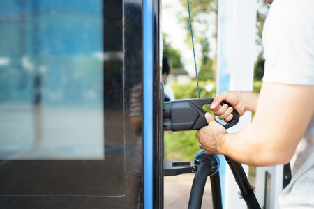 Handsome Asian young man holding an EV plug connector and attaching onto the car, man plugged in the EV charging connector to the vehicle.の写真素材