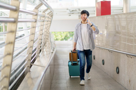 Asian young man dragging a suitcase along the city or airport terminal with shopping bags. Man traveling in the city or urban area.の写真素材
