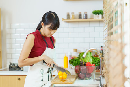 Happy cheerful beautiful Asian woman using cooking knife cutting a vegetables in kitchen. Woman preparing a vegan salad in kitchen.の写真素材