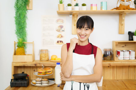 Happy cheerful beautiful Asian woman standing in a kitchen and smiling portrait. Lovely cute Asian girl cooking in kitchen.の写真素材
