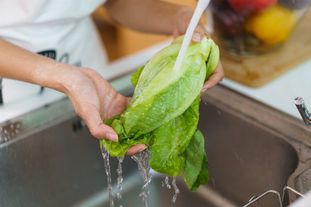 Happy healthy Asian woman washing a vegetables in domestic kitchen faucet before cooking. A housewife preparing and cleaning a fruits and vegetables carefully for cooking a healthy meal.の写真素材