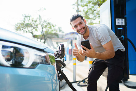 Handsome Asian young man holding an EV plug connector and attaching onto the car, man plugged in the EV charging connector to the vehicle.の写真素材