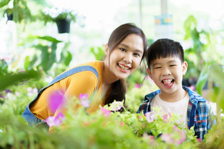 Happy Asian woman and little boy planting a house plants in green house together. Satisfied little boy enjoy planting and watering a small tree with his mother in greenhouse.の写真素材