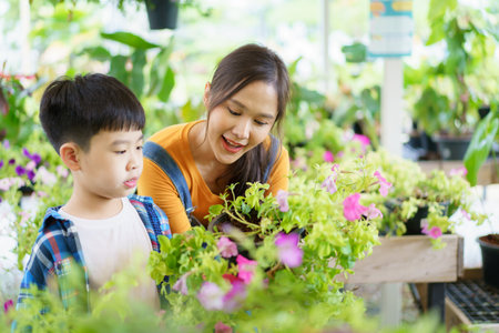 Happy Asian woman and little boy planting a house plants in green house together. Satisfied little boy enjoy planting and watering a small tree with his mother in greenhouse.の写真素材