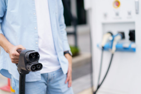 Unrecognizable Asian man holding AC type 2 EV charging connector at EV charging station, man...